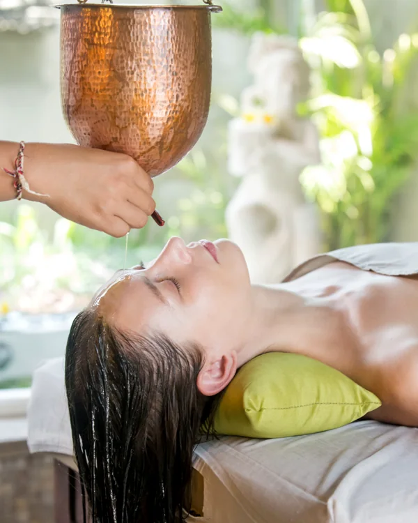 Shirodhara: warm oil poured over the forehead from a copper vessel